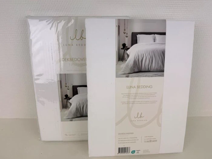 To pakker Luna Bedding-dynebetræk er udstillet på en hvid flade med billeder af en pænt redt seng med hvidt sengetøj på emballagen.