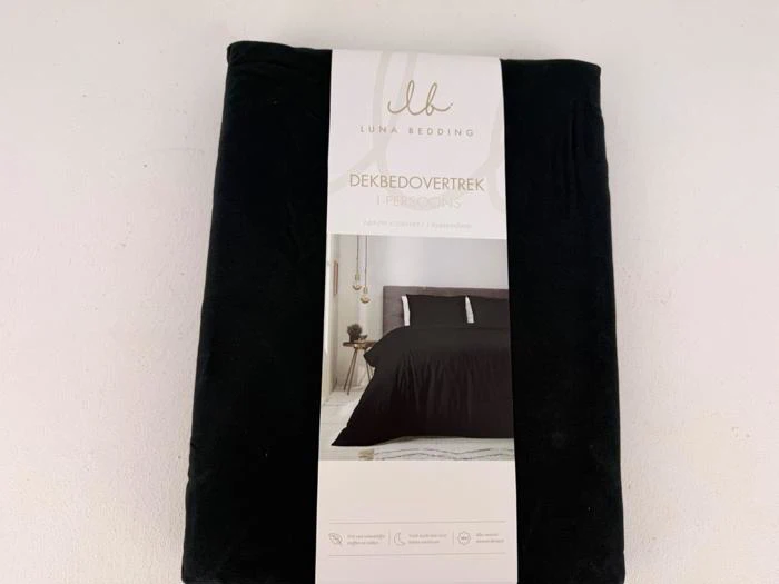 Et indpakket sort dynebetræk fra Luna Bedding, mærket DEKBEDOVERTREK 1-PERSOONS med et foto af en seng med en sort dyne på emballagen.
