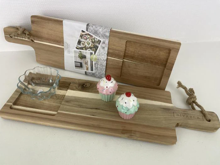 To serveringsbrætter af træ, et stående og et liggende, med et glasfad og to cupcakeformede keramikbeholdere på det liggende bræt.