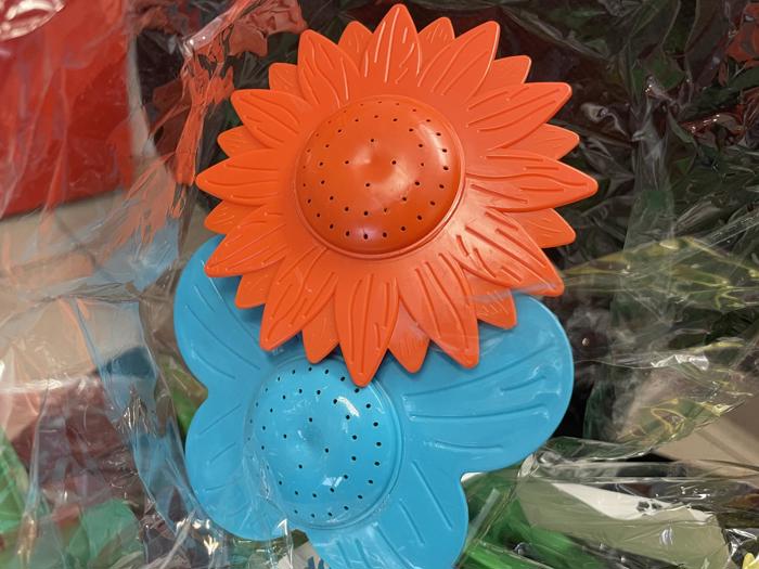 To tepotter af plast formet som blomster, en orange og en blå, med små huller til at trække i, placeret på en baggrund af klar plast.