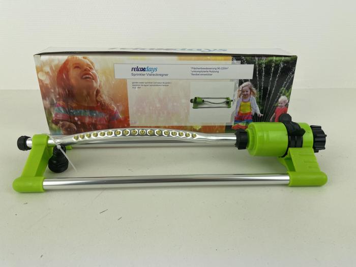 En oscillerende havesprinkler med grønne og sølvfarvede dele er udstillet foran sin kasse, som viser et smilende barn, der leger i vand.