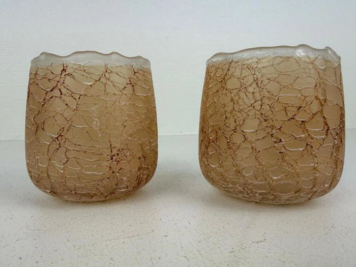 To beige glaskopper med en krakeleret, netlignende struktur på overfladen, placeret side om side på en lys flade mod en ensfarvet baggrund.