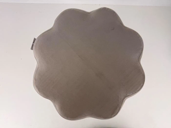Et billede oppefra og ned af en rund, grå pude med afskårne kanter, der hviler på en lys overflade.