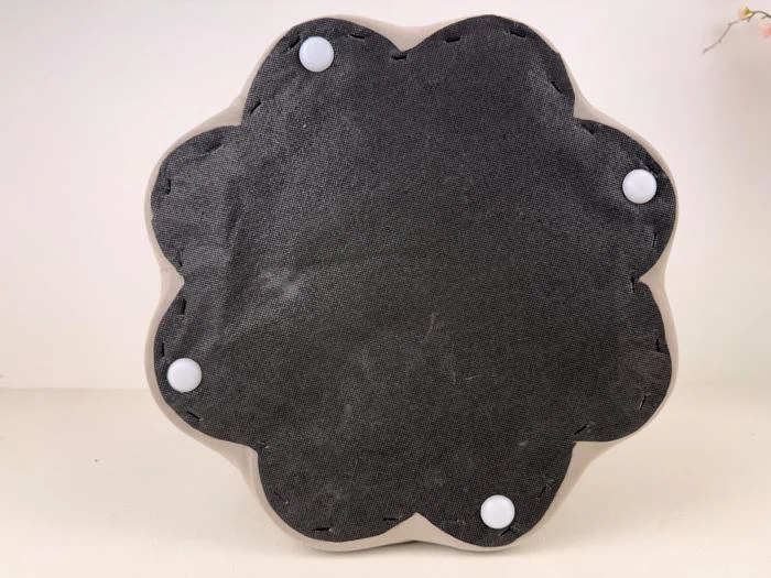 En rund, blomsterformet genstand med sort stofbund og fire hvide, runde fødder på en almindelig, lys baggrund.