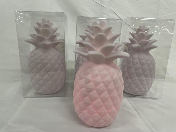 Tre pastelrosa, ananasformede objekter står på en hvid flade, to af dem i klare plastikkasser og en udenfor.