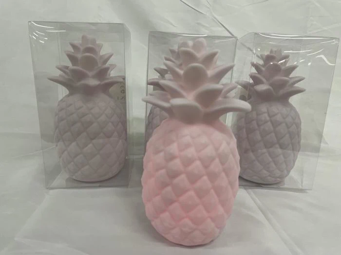 Tre pastelrosa, ananasformede objekter står på en hvid flade, to af dem i klare plastikkasser og en udenfor.