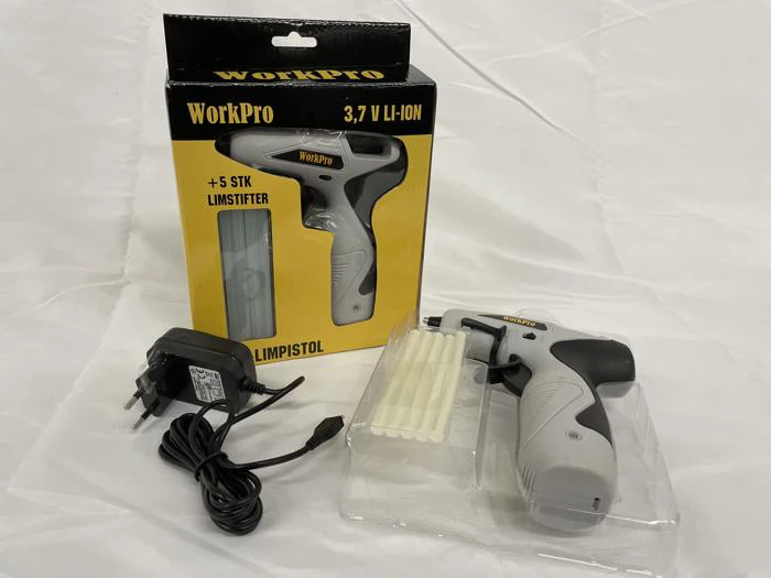 En trådløs grå WorkPro limpistol, oplader, limstifter og emballage er udstillet på en hvid overflade.