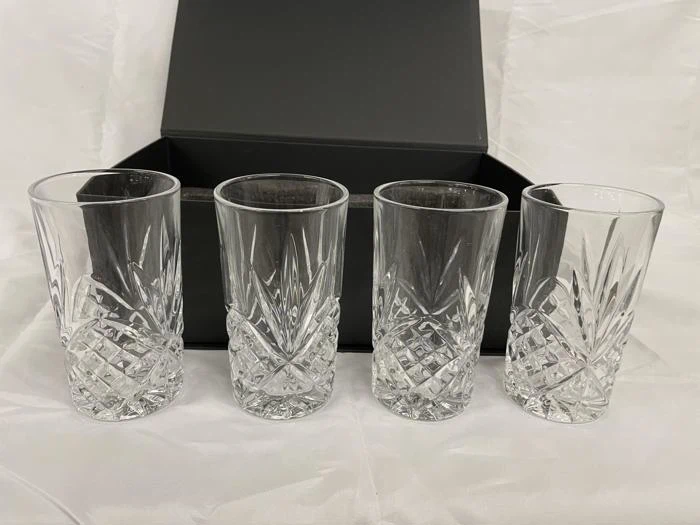 Fire drikkeglas i klar krystal med slebet glasmønster står foran en åben sort kasse på en hvid flade.
