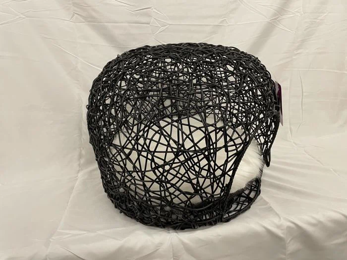 En hvid kat ligger sammenkrøllet og sover i en rund, sort, vævet trådseng på en lys stofbaggrund.