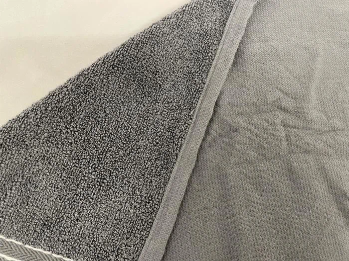 Et nærbillede af et gråt håndklæde, der viser den strukturerede, sløjfede frottéside og en glattere, flad underside med syede kanter.