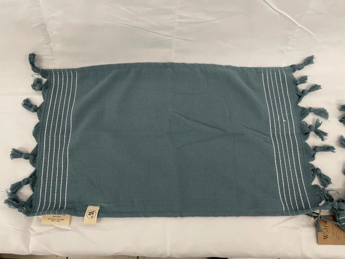 En blå rektangulær stofdækkeserviet med hvide syninger og kvaster på de korte sider, udstillet på en hvid stofoverflade.