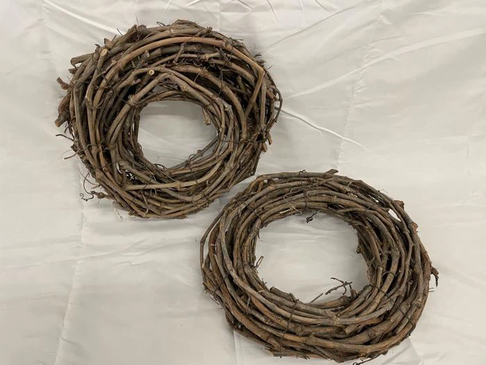 To cirkulære kranse lavet af sammenflettede nøgne grene eller ranker er placeret på en hvid stofbaggrund.