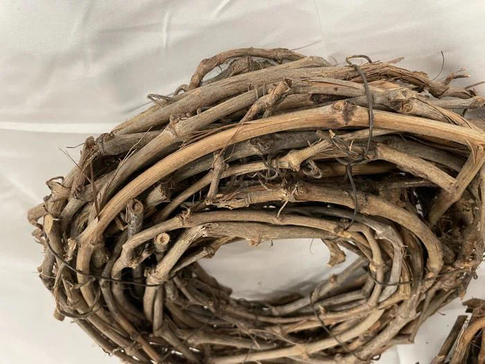 Et nærbillede af en cirkulær krans lavet af snoede, tørrede grene og lianer, der hviler på en hvid stofbaggrund.