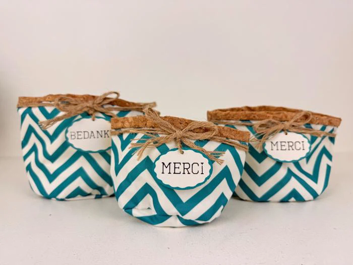 Tre små stofkurve med blå og hvide chevronmønstre og korkplader, hver mærket med en takkebesked på forskellige sprog: BEDANKT og MERCI.