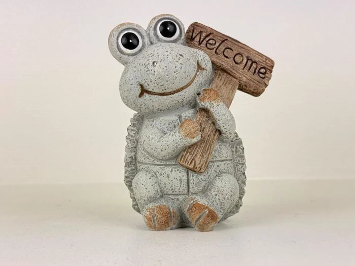 En sød stenfrø-figur, der holder et træskilt, hvor der står Welcome. Frøen smiler og har store, runde øjne.
