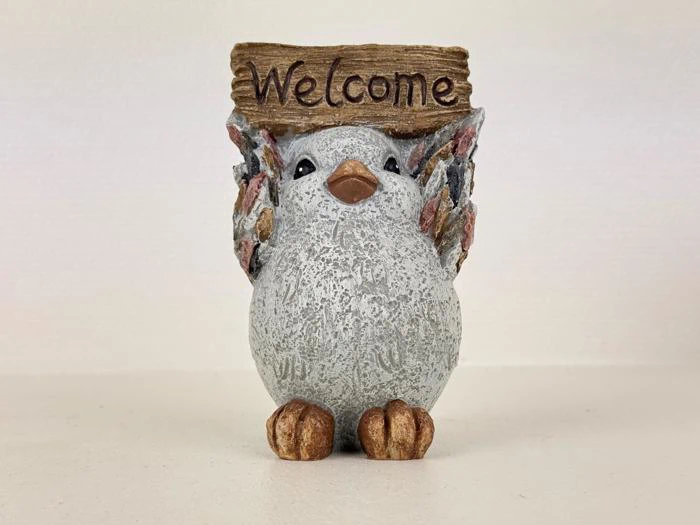 En lille fuglefigur, der holder et træskilt, hvor der står Welcome, med teksturerede vinger og fødder på en ensfarvet baggrund.