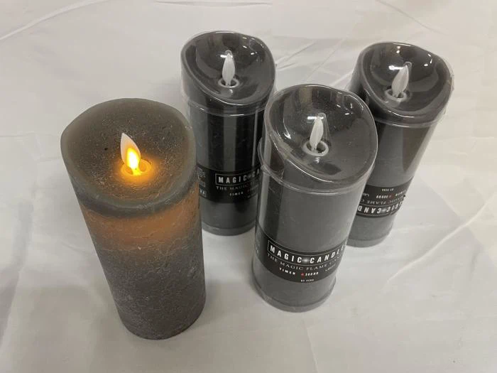 Der vises fire grå bloklys, tre indpakket i plastik og et uindpakket og tændt med en falsk flamme, der hviler på en hvid baggrund.