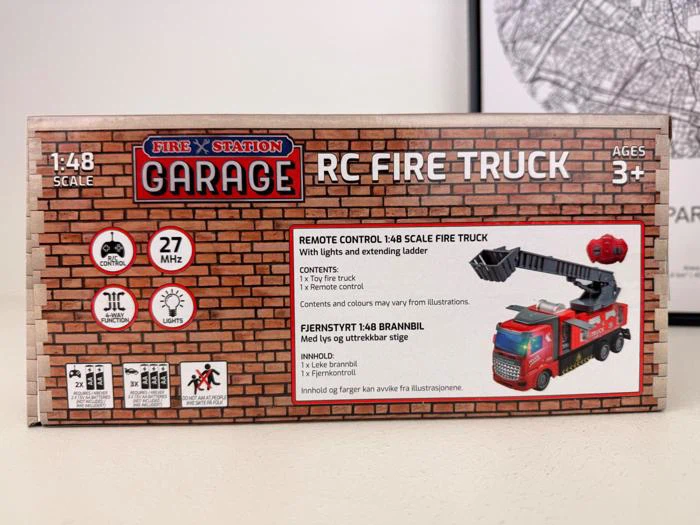 Æske med en fjernstyret brandbil til børn fra 3 år med billeder af den røde brandbil og produktinformation på en murstensmønstret baggrund.