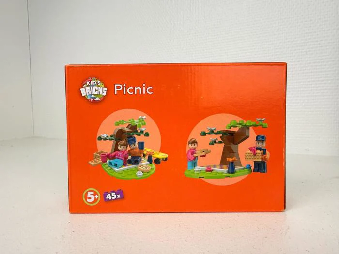 En orange æske mærket Kids Bricks Picnic viser legetøjspicnic og træscener med figurer, for 5+ år og 45 dele.