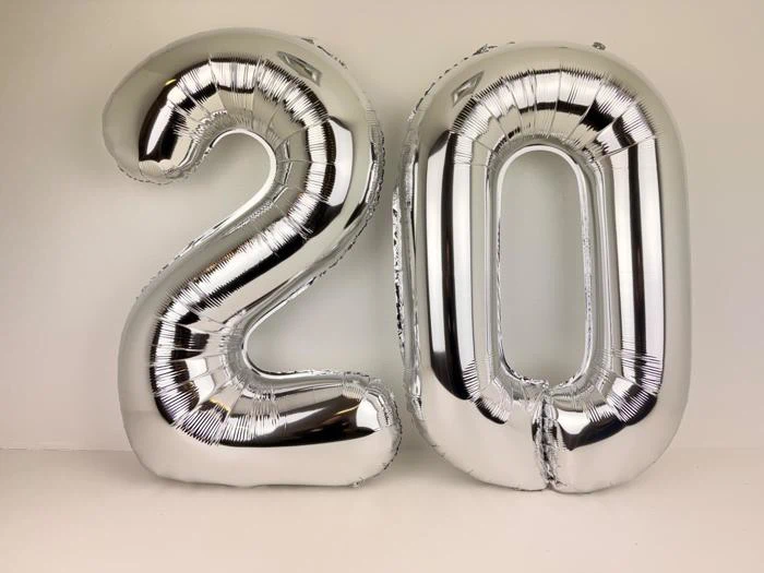 To store sølvfarvede folieballoner formet som tallet 20, der står på en almindelig lys baggrund.