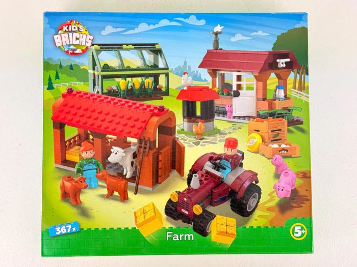 Æske til et "Kids Bricks"-bondegårdslegesæt, der viser en lade, dyr, bondegårdsfigurer, traktor, drivhus og landbrugsbygninger med en farverig bondegårdsscene i baggrunden.