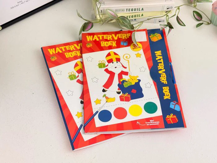 To farverige akvarelbøger til børn med en Sinterklaas-illustration på omslaget, placeret på en hvid flade ved siden af nogle grønne planter og stablede bøger.