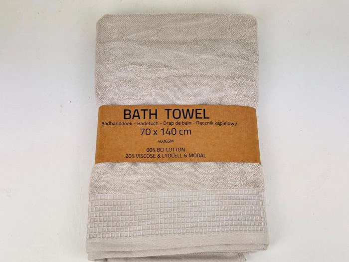 Et foldet beige badehåndklæde med en brun etiket, hvor der står BATH TOWEL 70 x 140 cm, 80% bomuld, 20% viskose & lyocell & modal på flere sprog.