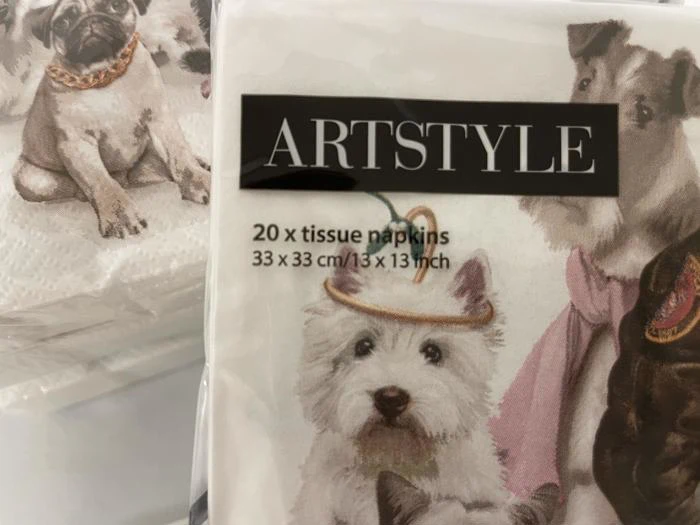 En pakke ARTSTYLE-servietter med illustrationer af hunde, bl.a. en hvid hund med en lille festhat. Teksten lyder som følger: 20 x stofservietter 33 x 33 cm/13 x 13 tommer.