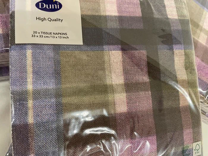 En pakke med 20 Duni-servietter af høj kvalitet med ternet mønster i lilla, beige, rosa og grøn, indpakket i klar plastemballage.