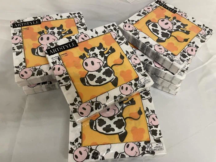 Pakker med Artstyle-servietter med en tegneserieko med gul baggrund og orange pletter, stablet på en hvid overflade.