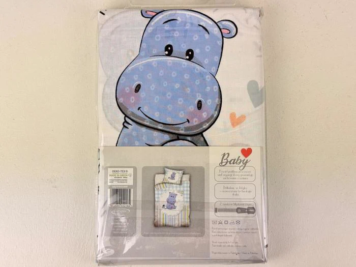 Emballeret babysengesæt med en stor, smilende blå tegneserieflodhest og pastelfarvede hjerter på betrækket. Et mindre billede nedenfor viser sengesættet på en tremmeseng.