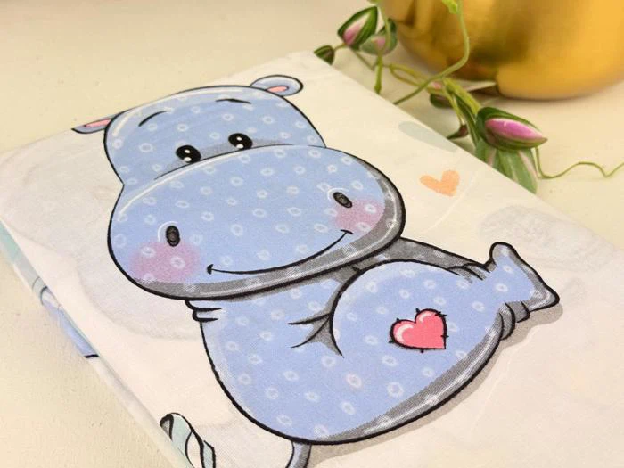 En sød tegneserieflodhest med et lyserødt hjerte på maven er trykt på stof ved siden af en guldkrukke med grønne ranker og lyserøde knopper.