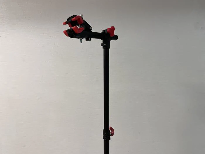 Et sort stativ med røde klemmer og justeringsknapper, opstillet mod en almindelig lys væg.