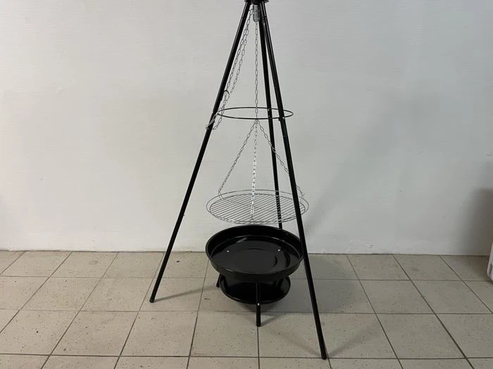 En sort metalstativgrill med en hængende rund rist over en sort skål, der står på et flisegulv mod en almindelig hvid væg.