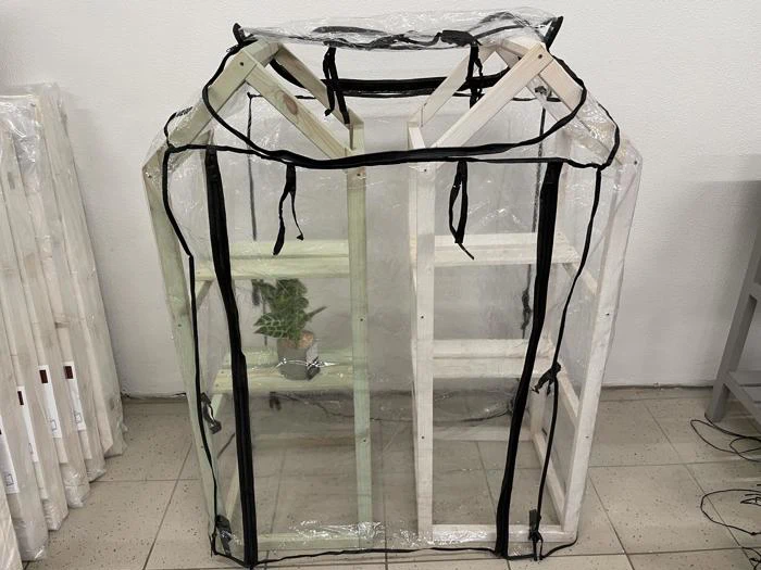 En lille træreol dækket af et drivhus i klar plast med sort kant og med en enkelt potteplante indeni.