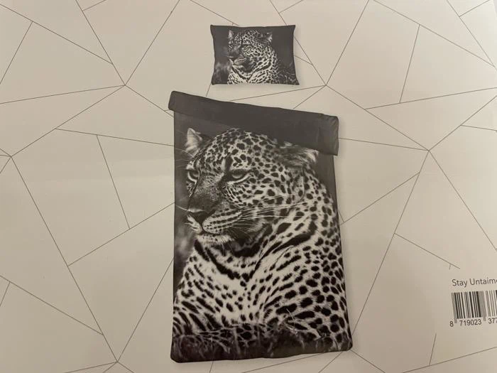 Et sengesæt med et realistisk sort-hvidt leopardprint består af et pudebetræk og et dynebetræk på en geometrisk mønstret baggrund.