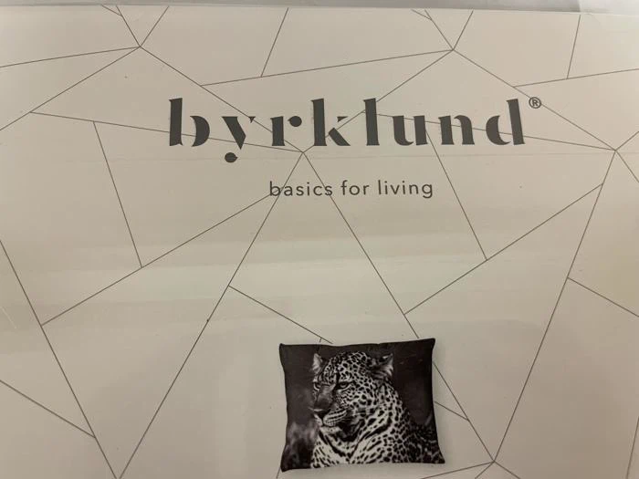 Produktemballage med mærkenavnet byrklund, taglinen basics for living og et billede af en pude med leopardprint.