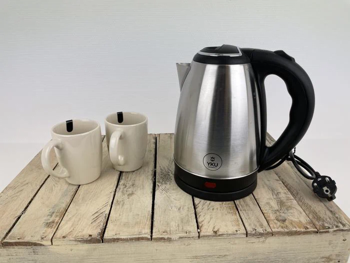 En elkedel i rustfrit stål og to hvide keramikkrus står på en rustik træoverflade, hvor elkedlen er tilsluttet og klar til brug.