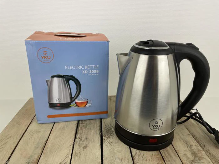 En elkedel i rustfrit stål med et sort håndtag er sat til ved siden af den blå og orange kasse, som viser et billede af elkedlen og en kop te.