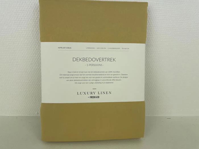 Et pakket dynebetræk til én person fra Luxury Linen, indpakket i brunt papir med hollandsk tekst og produktoplysninger på forsiden.