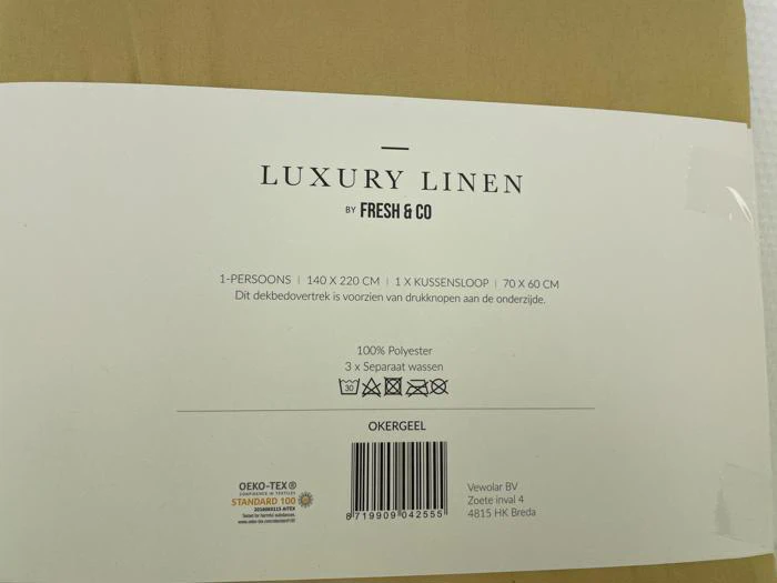Etiket til luksus sengetøjssæt i hør fra Fresh & Co i okker. Detaljer omfatter størrelse, materiale (100 % polyester), plejesymboler og OEKO-TEX STANDARD 100-certificering.