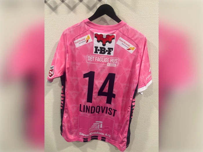 En lyserød sportstrøje med nummer 14, navnet LINDQVIST og forskellige sponsorlogoer på ryggen, hængende på en bøjle.