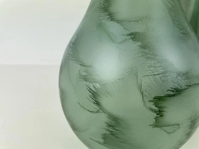 Nærbillede af en grøn, matteret glasvase med strukturerede, penselstrøgslignende mønstre på overfladen.