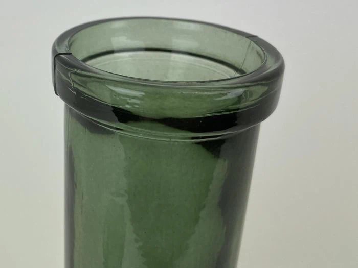 Nærbillede af kanten af en grøn glasvase med et lille skår på kanten, sat mod en almindelig baggrund.