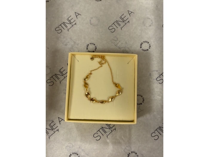 En guldkæde med snoede led ligger i et åbent cremefarvet smykkeskrin på STINE A-mærket indpakningspapir.