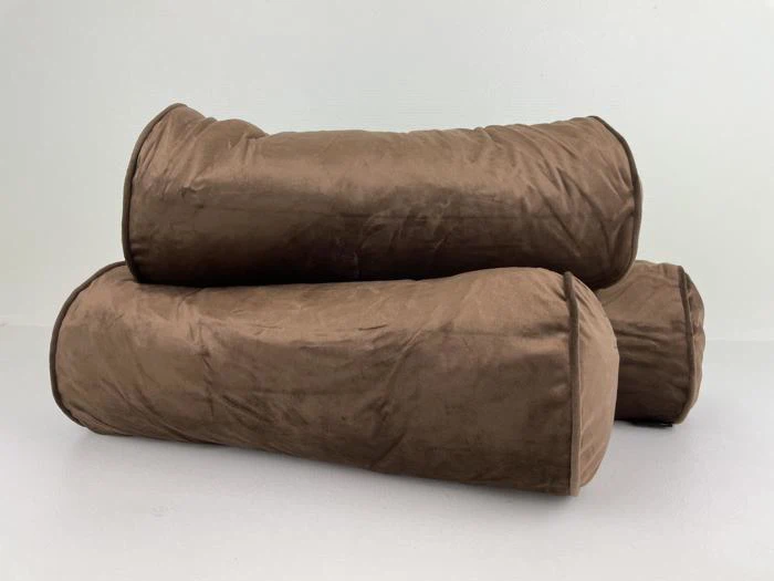 To store, cylindriske brune bolsterpuder er stablet oven på hinanden på en almindelig hvid overflade mod en hvid baggrund.