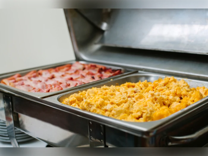 En buffetbakke med røræg i det ene rum og kogte baconstrimler i det andet, begge dele holdt varme i pander af rustfrit stål.