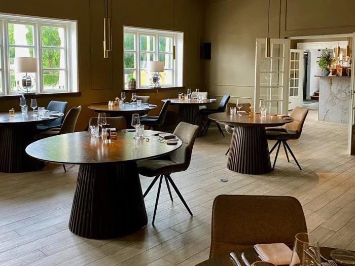 En moderne, elegant restaurantspisestue med runde borde, moderne stole, opdækning, store vinduer og naturligt lys.