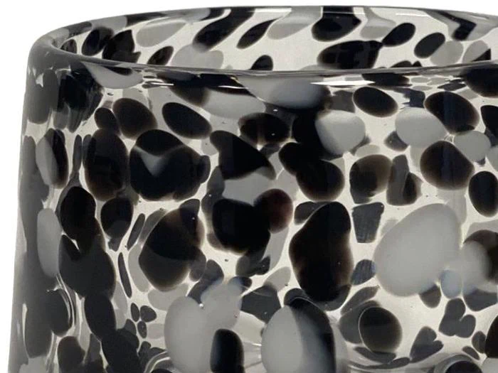 Nærbillede af en glasbeholder med et sort og hvidt plettet mønster på en gennemsigtig baggrund.