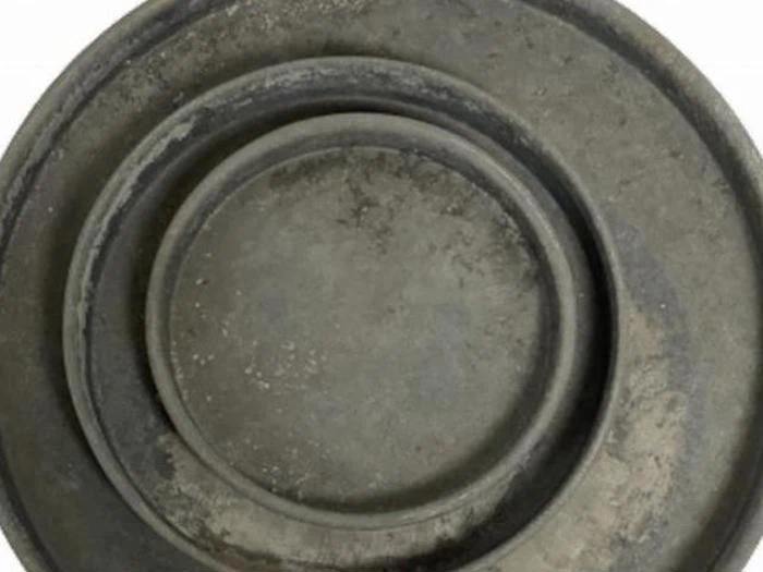 Tre stablede, runde, forvitrede metalplader set ovenfra, der viser et cirkulært, lagdelt mønster med en mat grå overflade.